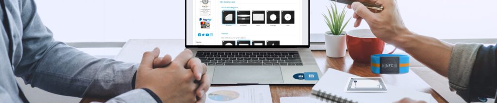Business meeting with laptop showing an NFC product configurator, NFC cards, and a wristband on a desk.