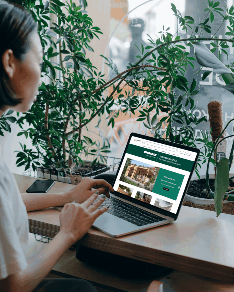 Person browsing the HolzLand Becker online shop on a laptop in a bright indoor setting with plants.