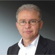 Professional headshot of a man wearing glasses, a white shirt, and a dark blazer.